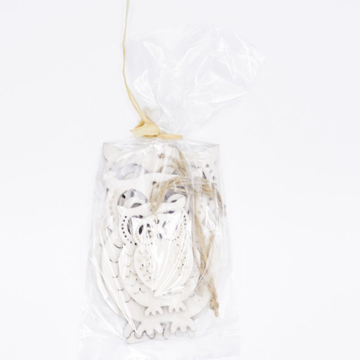Décoration en bois blanc, ornée, emballée dans un sachet transparent.