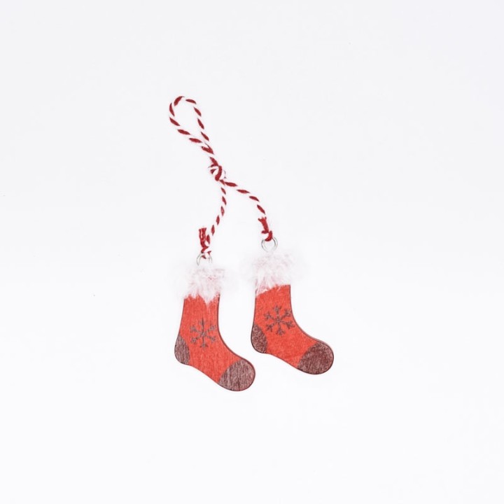 Petits chaussons de Noël rouges avec pompons blancs, suspendus par une corde tressée.