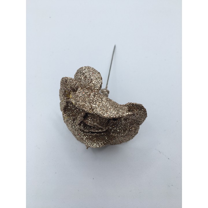 Broche en forme de visage, recouverte de paillettes dorées, sur fond blanc.
