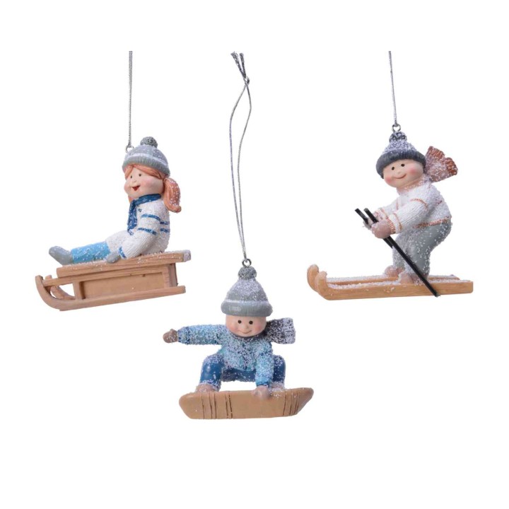 Trois figurines d'enfants en hiver, jouant avec des luges et des skis, décorées de paillettes.