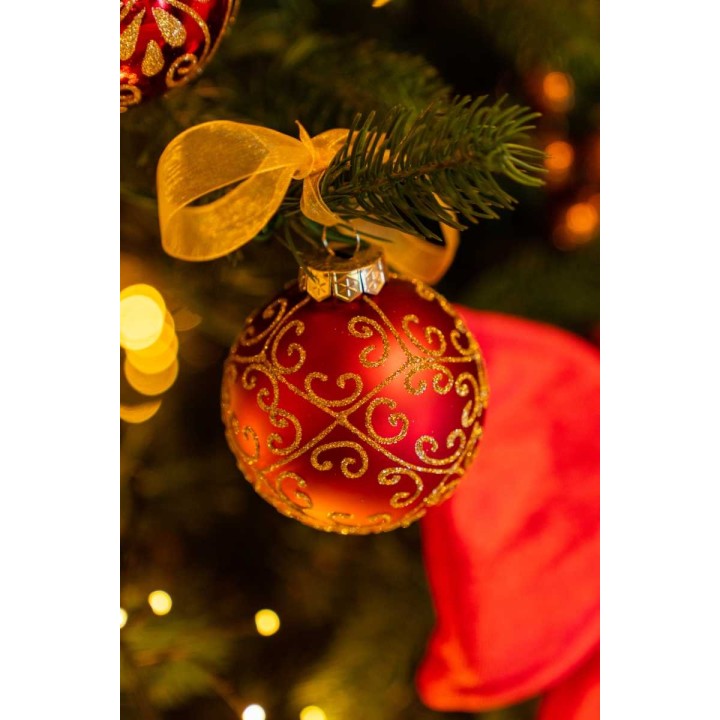Boule de Noël rouge ornée de motifs dorés, suspendue à un sapin, avec un nœud en satin.