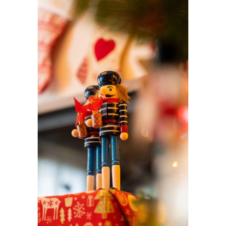 Deux soldats en bois colorés, décorés pour Noël, entourés de guirlandes festives.