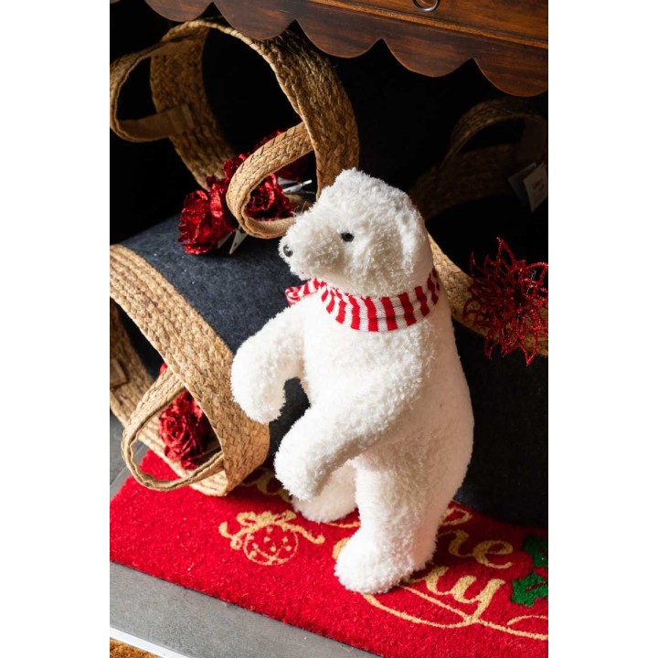 Ours polaire en peluche, portant une écharpe rayée, devant des décorations festives.