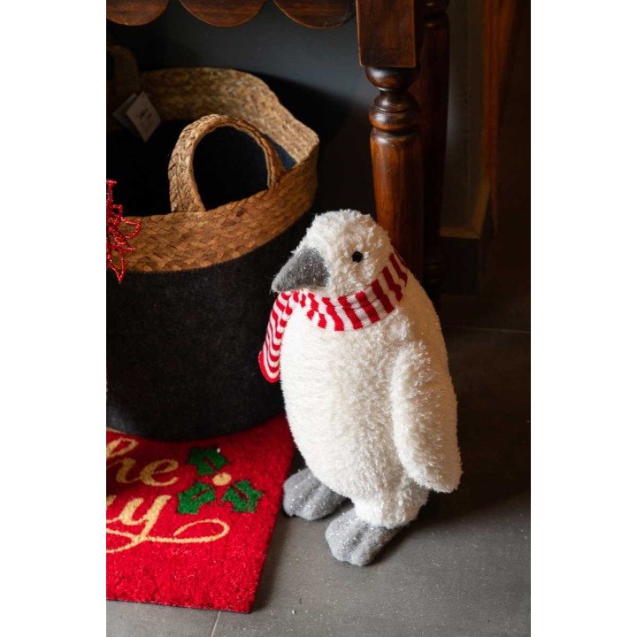 Pingouin en peluche blanc avec écharpe rouge et blanche, posé près d'un panier tressé.