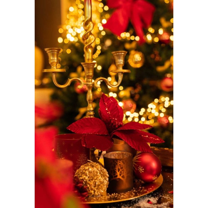 Bouquet de Noël avec bougeoir doré, décorations rouges et éclairage chaleureux.