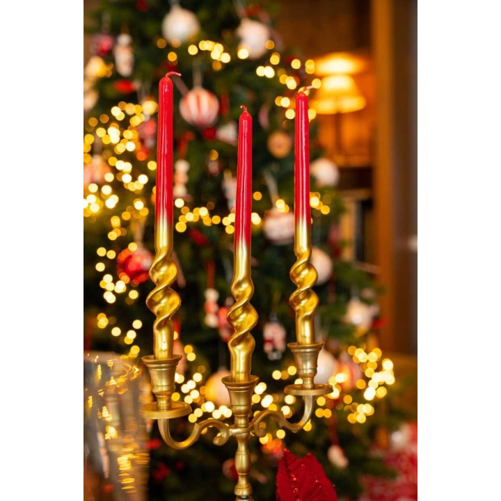 Bougeoir doré avec trois bougies rouges, décorations festives en arrière-plan.