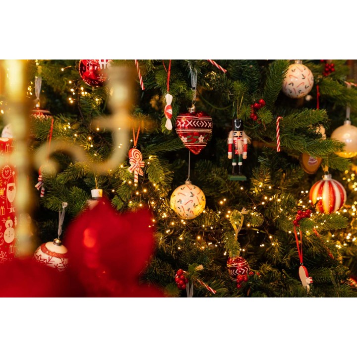 Ornements colorés et guirlandes lumineuses décorent un sapin festif. Atmosphère chaleureuse.