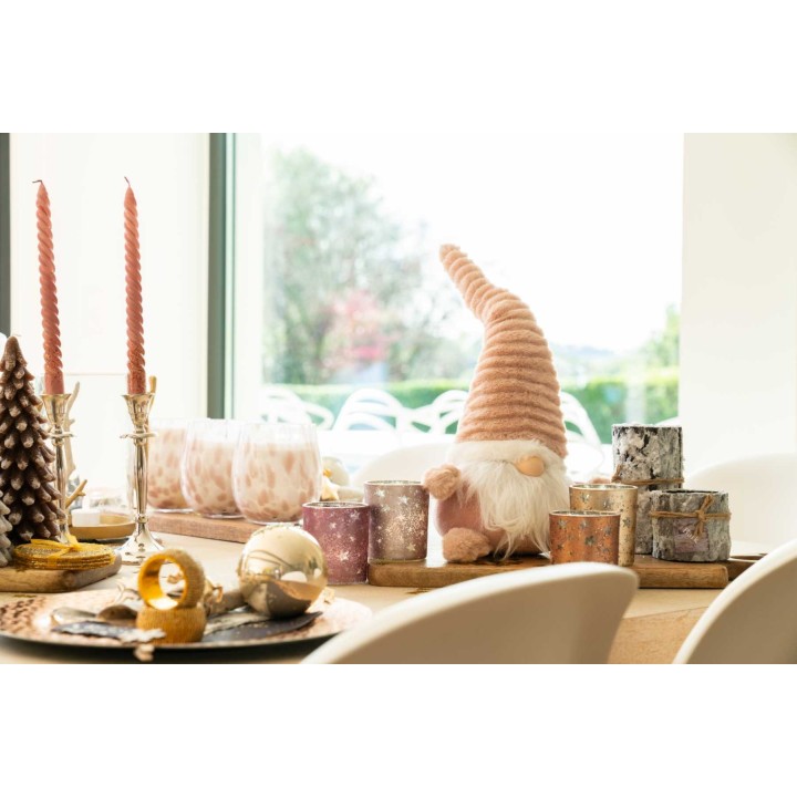 Ambiance festive avec bougies, décorations dorées et un gnome en peluche sur une table lumineuse.