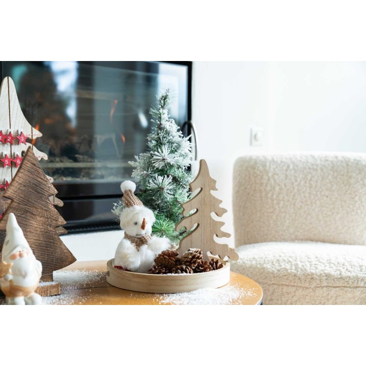 Décor festif avec sapins en bois, un bonhomme de neige et des cônes de pin sur une table.