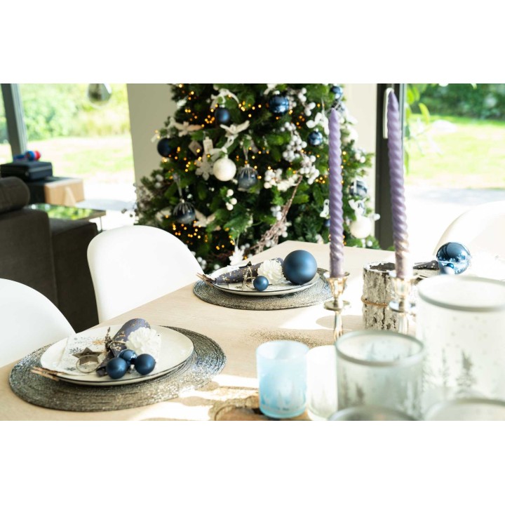 Table élégamment dressée avec des décorations bleues, bougies et un sapin festif en arrière-...