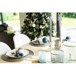 Table élégante avec décorations bleues, chandelles violettes et sapin festif en arrière-plan.