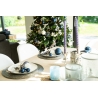 Table élégante avec décorations bleues, chandelles violettes et sapin festif en arrière-plan.