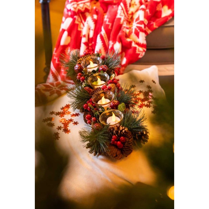 Bougies décorées de branches et pommes de pin, sur tissu clair, entourées de flocons rouges.