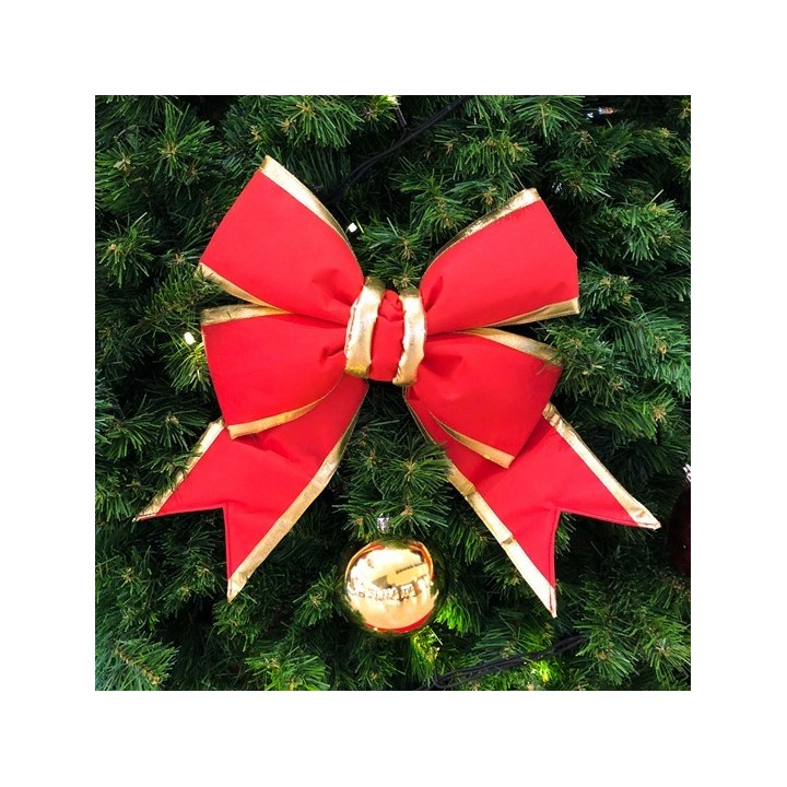 Grand nœud rouge avec dorures sur un sapin de Noël, entouré de branches vertes.