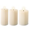 Trois bougies blanches cylindriques allumées, éclairant doucement un environnement calme.