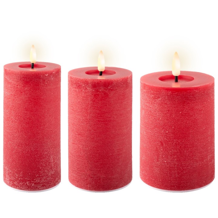 Trois bougies cylindriques rouges, allumées, diffusent une douce lumière chaleureuse.