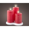 Trois bougies cylindriques rouges, allumées, sur un socle blanc, créant une ambiance chaleureuse.