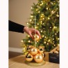 Main plaçant des boules dorées sur une base scintillante, devant un sapin illuminé.