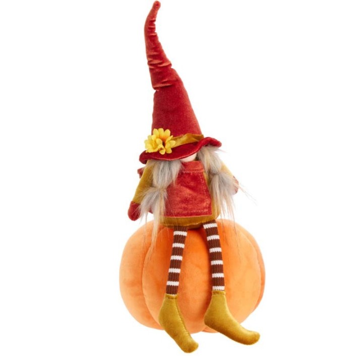 Poupée aux cheveux longs, chapeau rouge, assise sur une citrouille orange, style automnal.