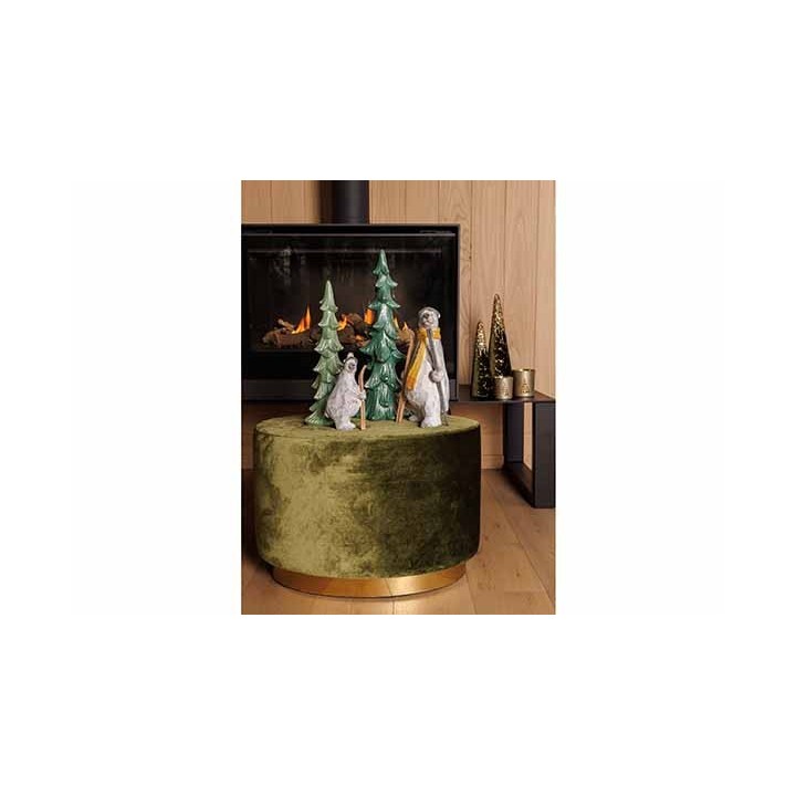 Décor cozy avec animaux en céramique et sapins, sur un pouf en velours vert près d'un feu.