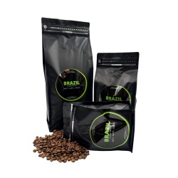Trois sachets noirs de café en grains, entourés de grains éparpillés. Étiquettes vertes.