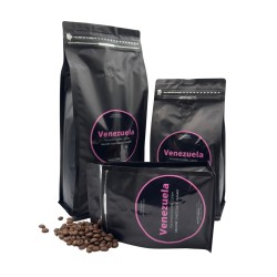 Trois sachets noirs de café avec étiquettes roses, entourés de grains de café.
