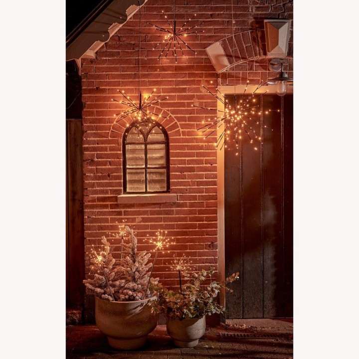 Mur en briques illuminé, décoré de lumières scintillantes et de plantes hivernales.