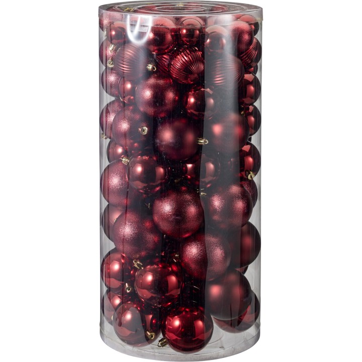 Boules de Noël rouges brillantes et mates, empilées dans un cylindre transparent.